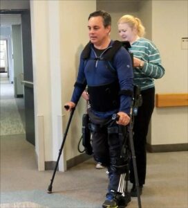 A research participant with spinal cord injury walks in the Ekso GT assisted by a physical therapist